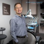 Dr. Luis Camach profile and invisalign picture of waist up with dental chair behind him.